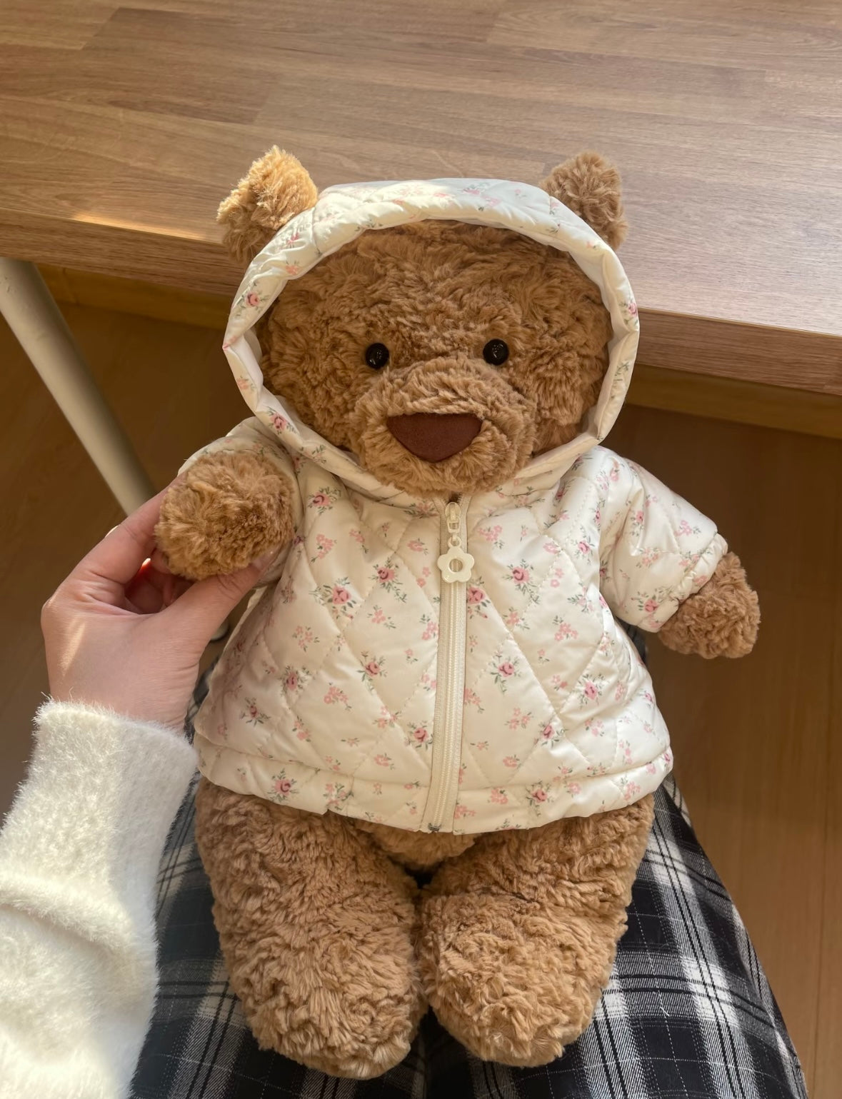Brown teddy bear wearing cream floral puffer jacket with hood, held up