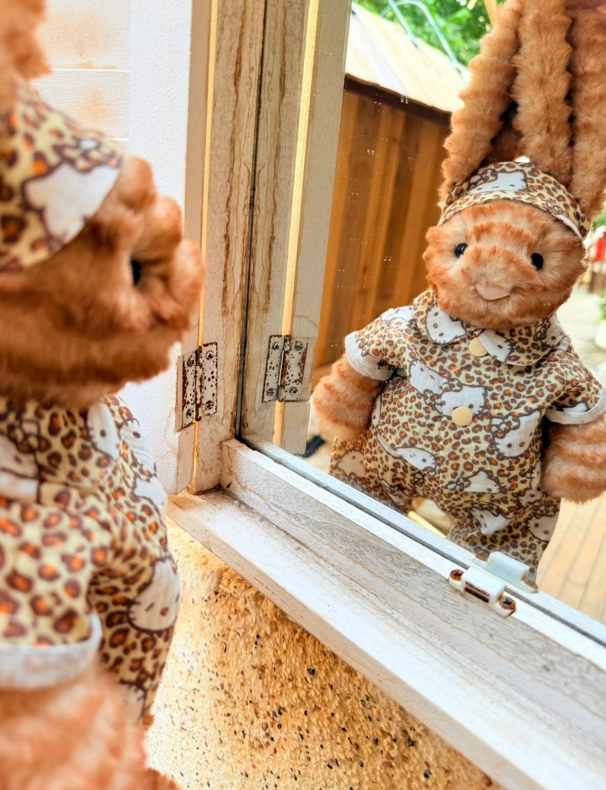Jellycat bunny wearing Hello Kitty leopard print outfit, reflected in window