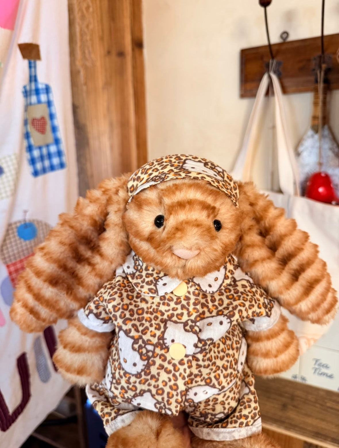 Jellycat bunny wearing Hello Kitty leopard print three-piece set, front view indoors