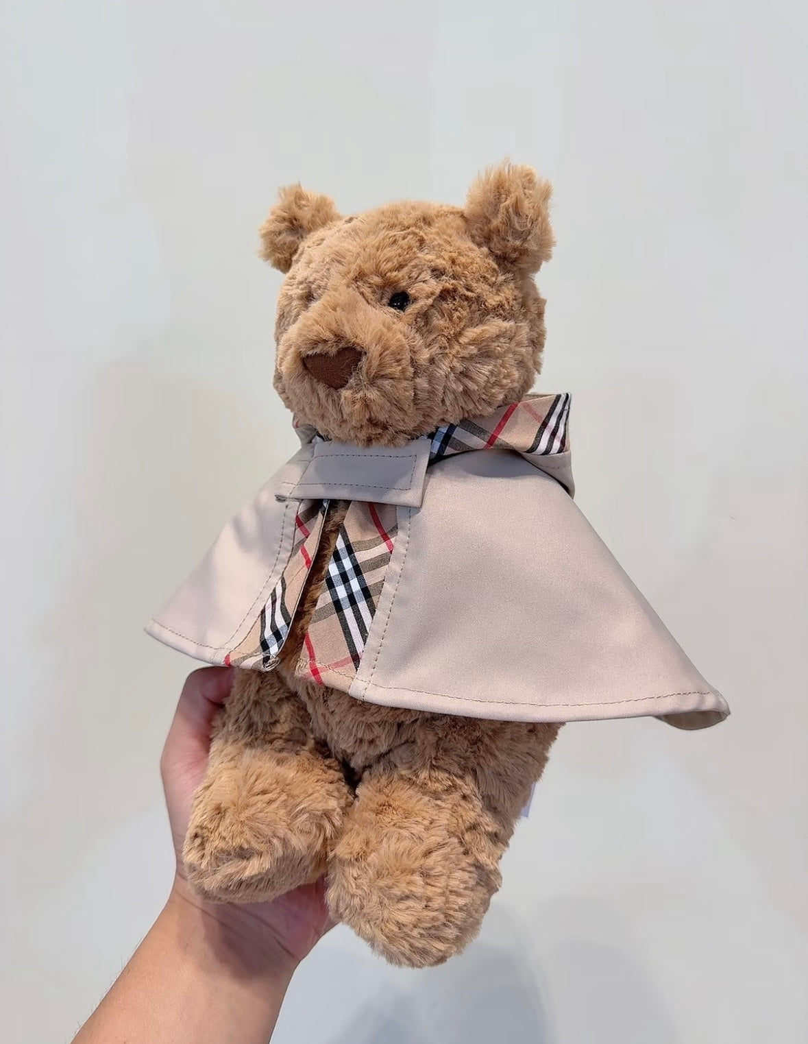 White plush terrier wearing a stone trench cape with check-lined collar and scarf