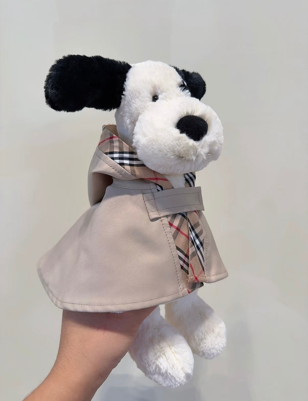 Beige plush puppy wearing a trench cape with check lining and neck tab