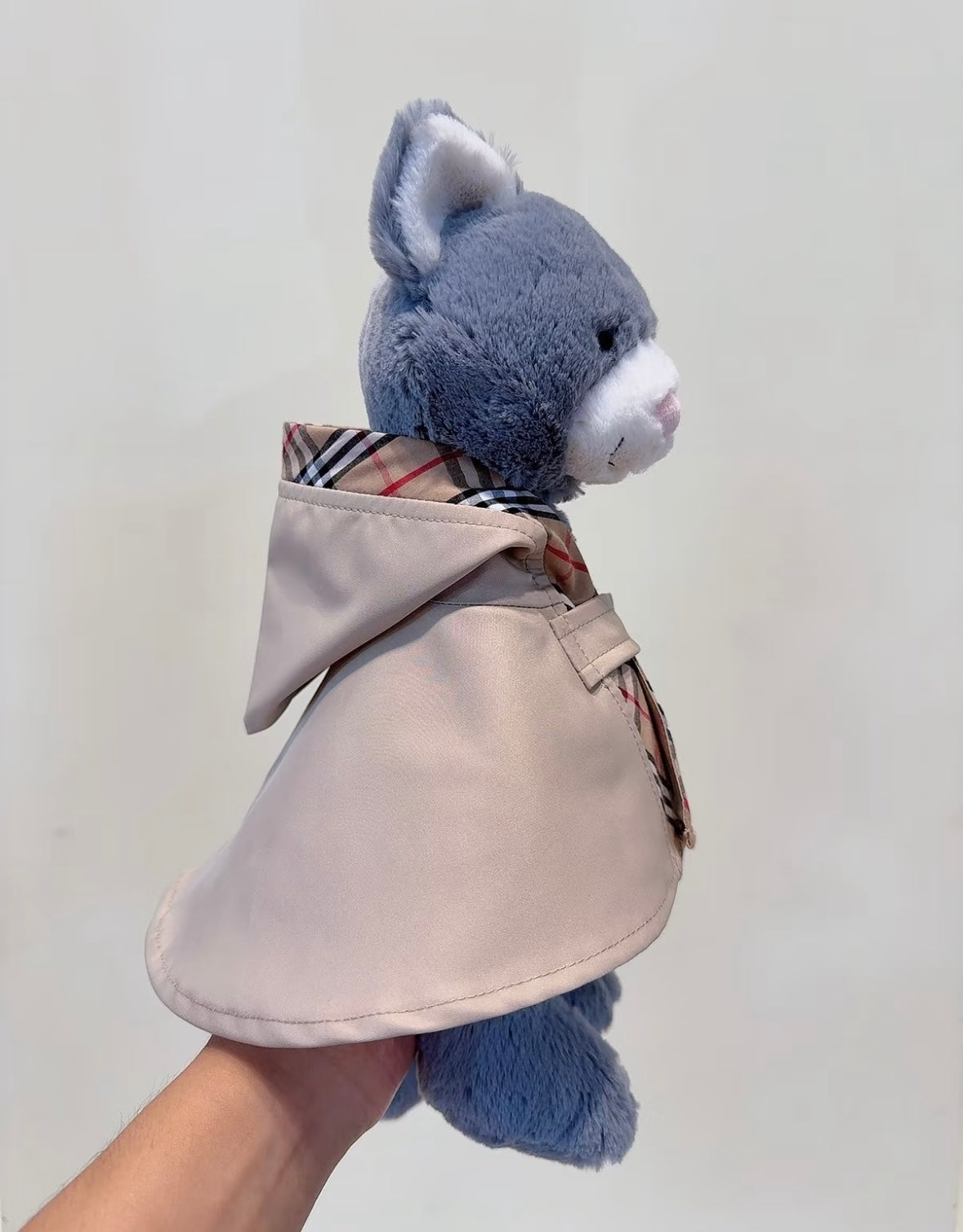 Golden teddy bear wearing a stone trench cape with a check scarf tied at the neck