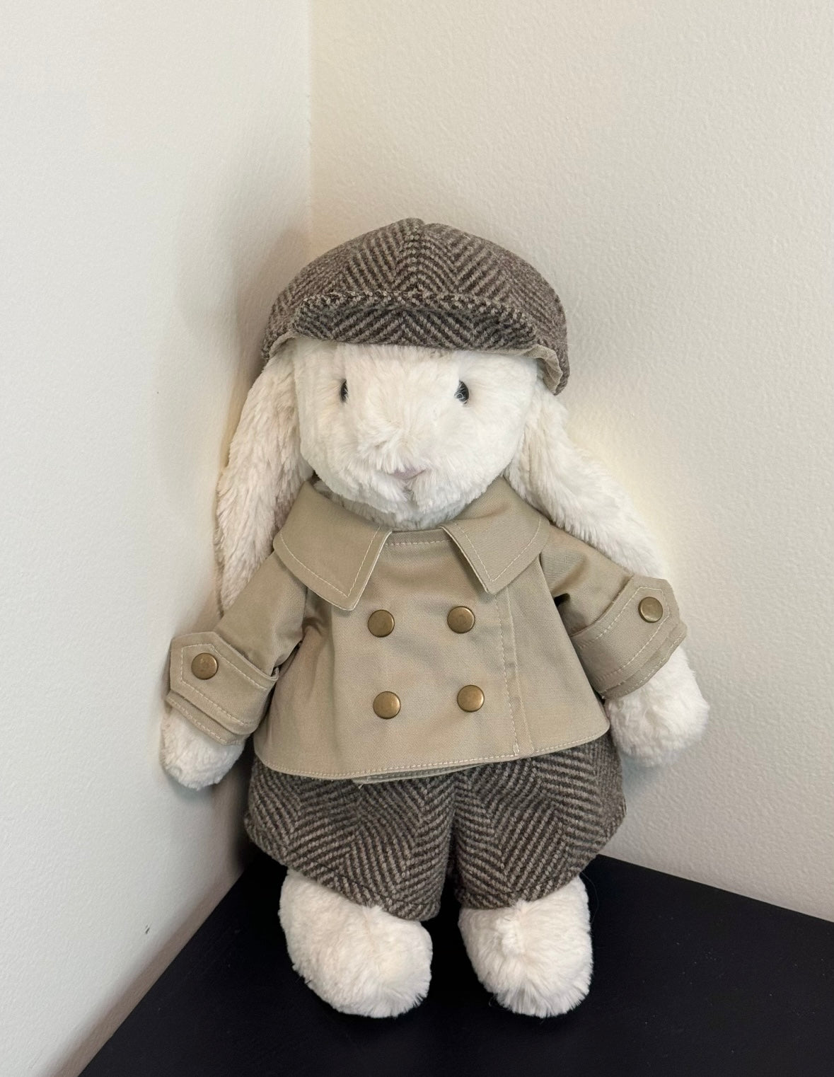 Bashful Bunny wearing cream trench coat, grey herringbone trousers and flat cap, front view